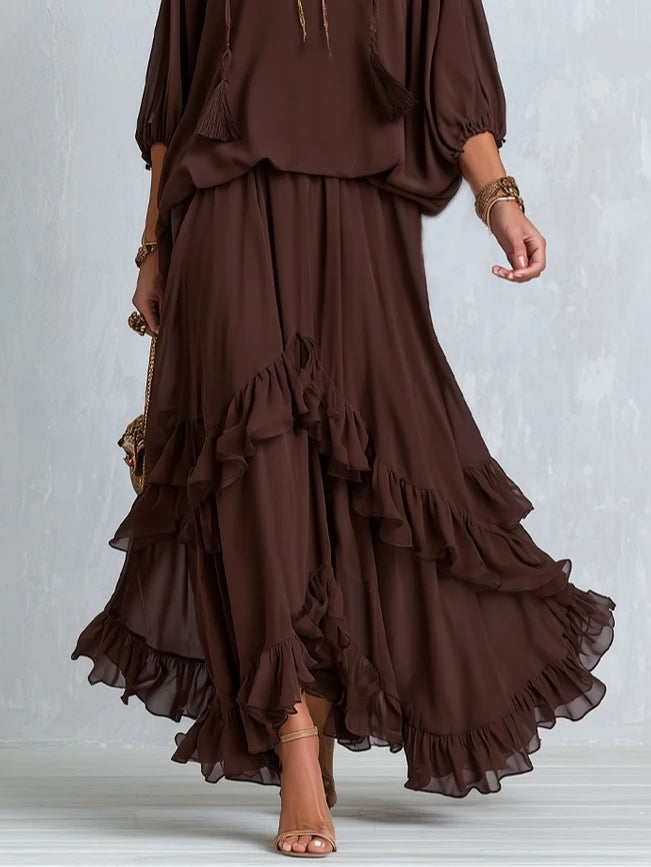 Close-up of brown ruffled layered skirt with chiffon top, worn by a woman with sandals, against a light backdrop.