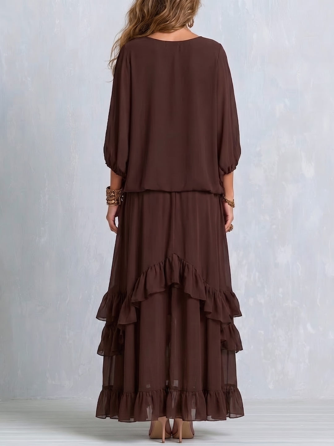 Back view of brown chiffon top and ruffled layered skirt set, worn by a woman, against a textured light background.