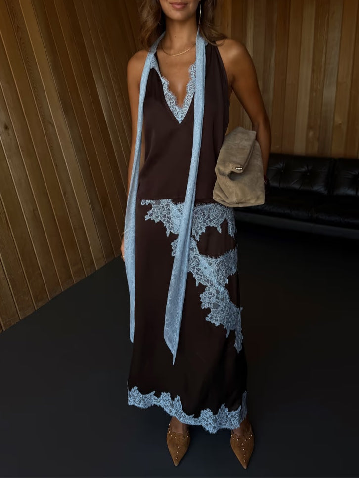 Woman in halter lace suit with blue details, holding plush beige clutch in a wooden room.