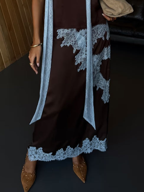 Partial view of lace suit with blue accents and studded brown shoes on wooden floor.