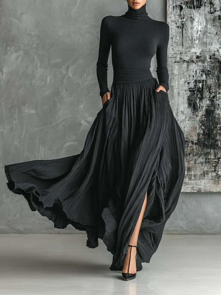 Elegant black turtleneck and pleated skirt set. Flowing skirt with slit, worn with high heels. Studio background.