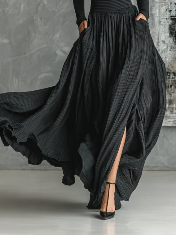 Close-up of pleated black skirt with thigh-high slit. Paired with black high heels, studio background.