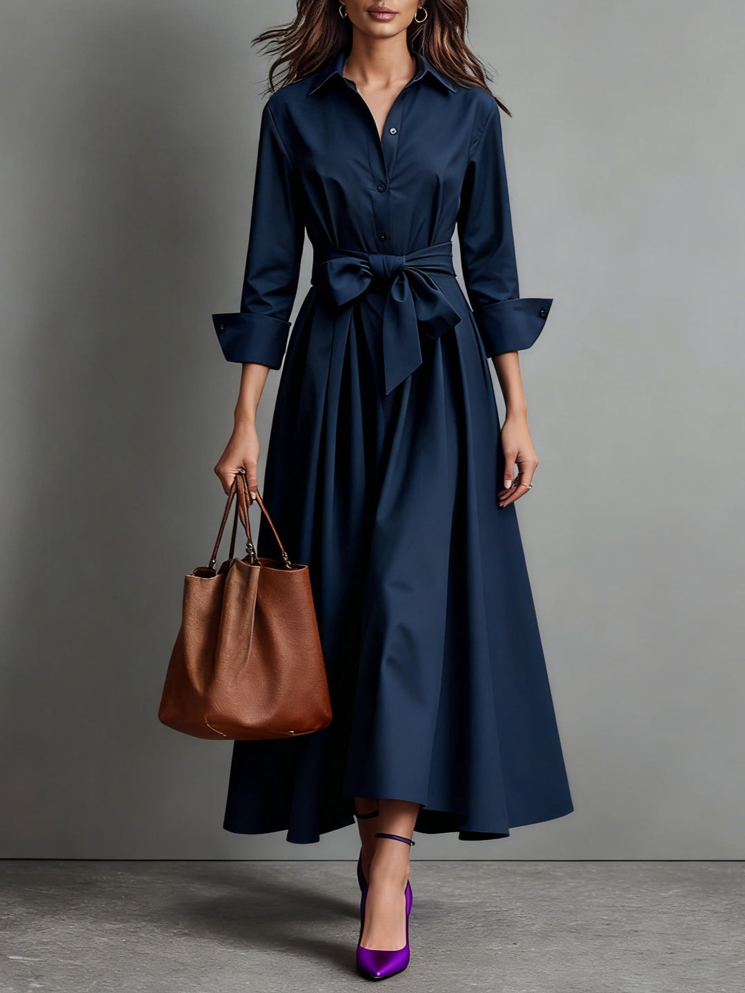 Navy maxi dress with waist belt, long sleeves, brown tote bag, and purple heels in a studio environment.