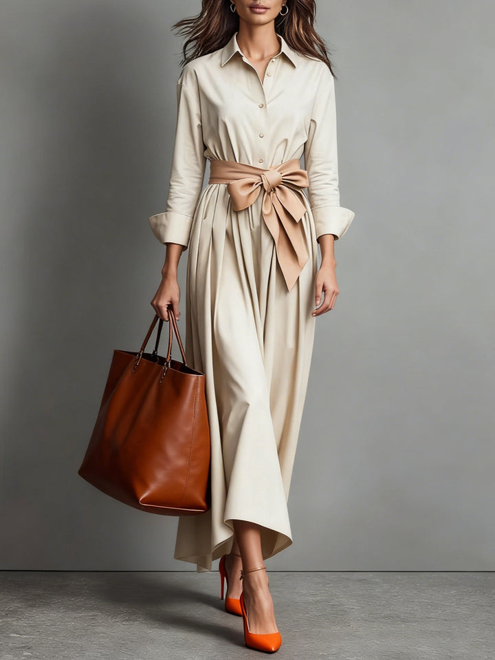 Beige maxi dress with waist belt, long sleeves, brown tote bag, and orange heels in a studio environment.