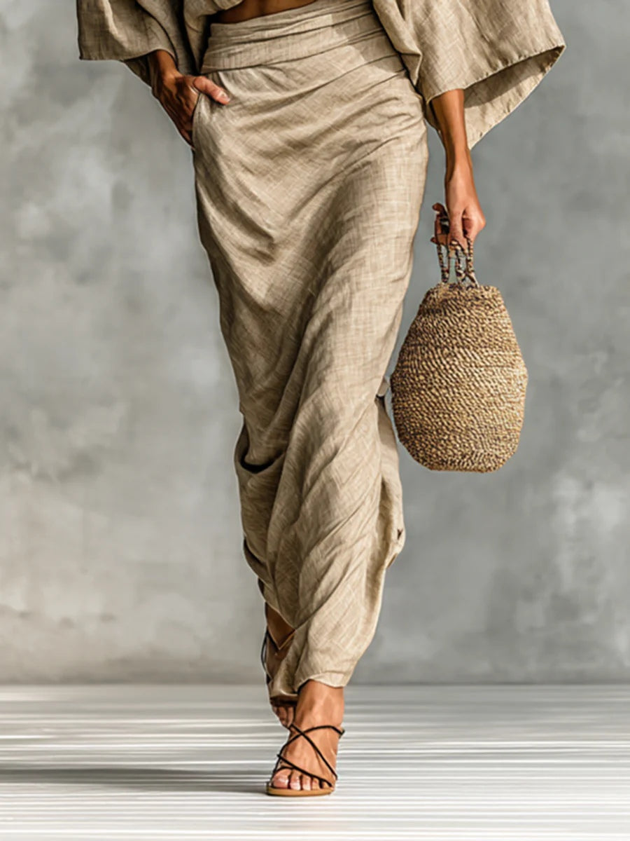 Elegant light brown draped skirt with strappy sandals and woven bag on striped floor surface.
