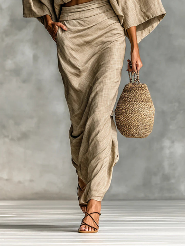Elegant light brown draped skirt with strappy sandals and woven bag on striped floor surface.