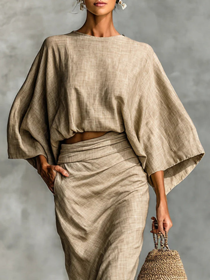 Close-up of woman wearing a light brown set with a flowy top and draped skirt, holding a woven bag.