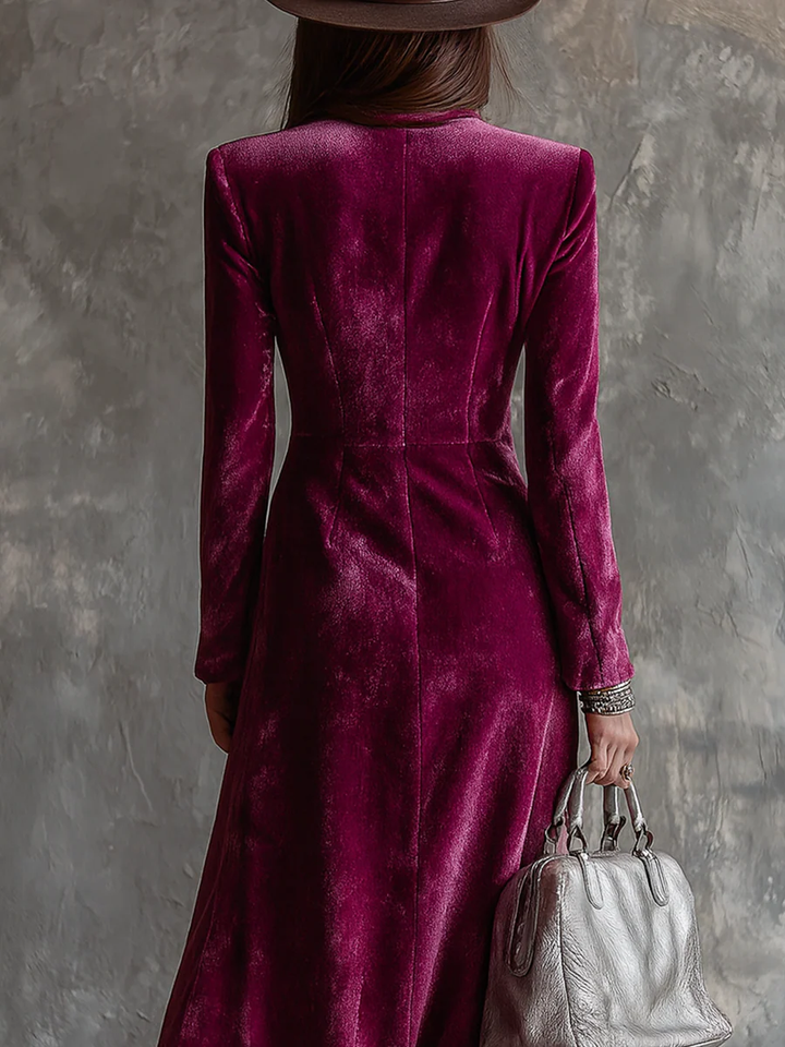 Back view of a deep pink long blazer dress worn by a woman, holding a silver bag, against a textured wall.