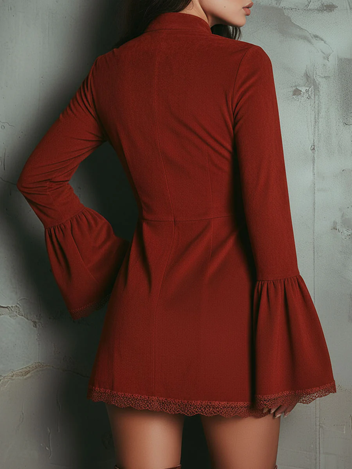 Back view of a red mini dress with flared sleeves and intricate embroidery, worn by a model against a textured wall.