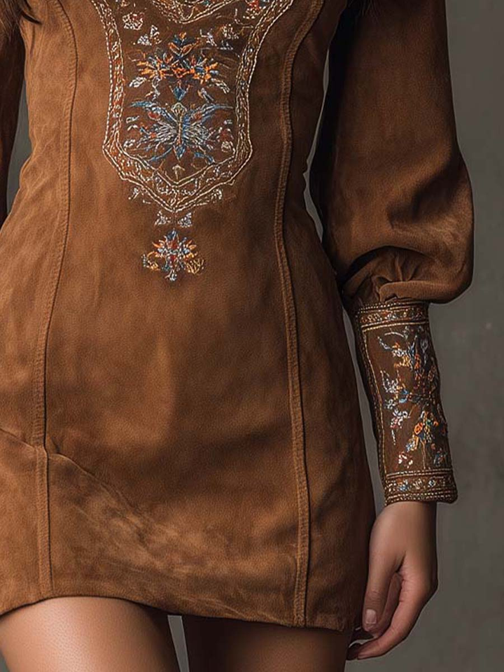 Detail of lower half of suede mini dress with floral embroidery on cuffs, set against a gray background.