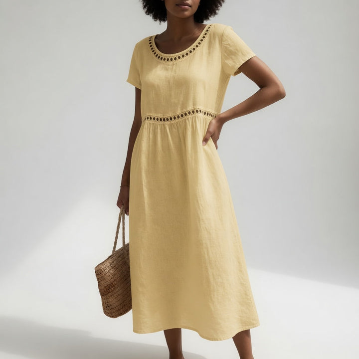 Yellow midi dress with eyelet trim, short sleeves, and an easy fit, worn by a person carrying a woven bag. Light studio background.