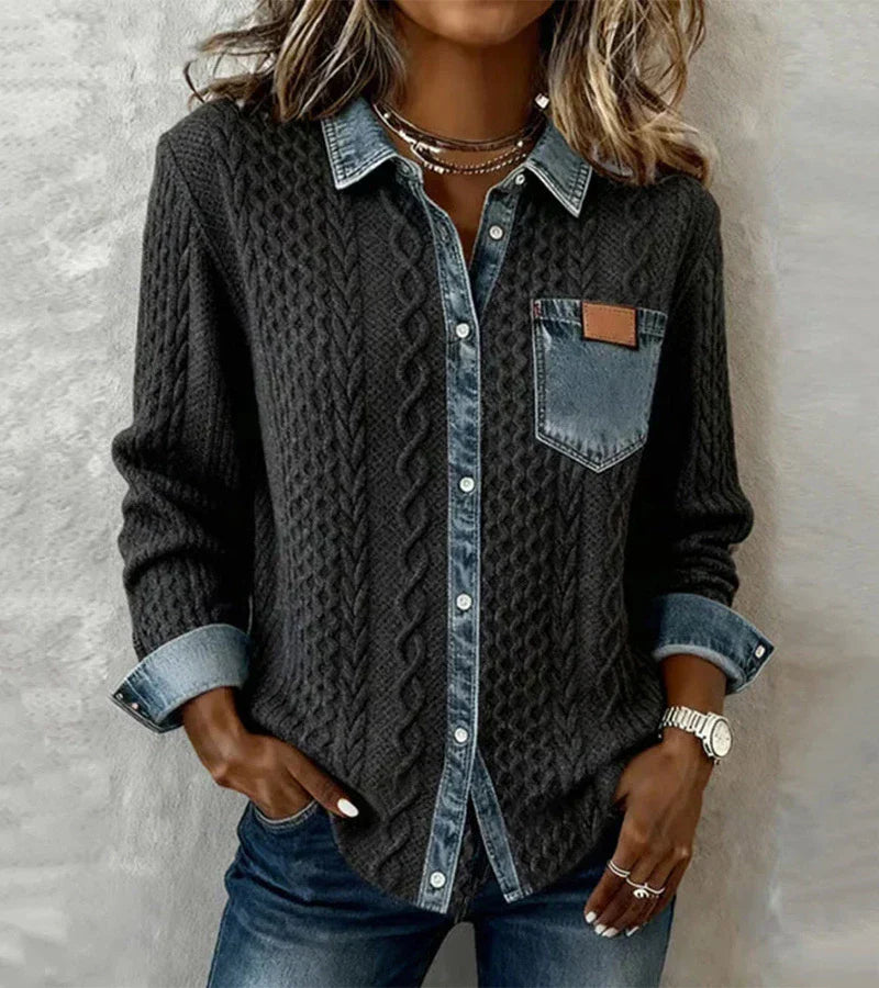 Person in a dark knit top with denim elements, standing before a textured gray surface.