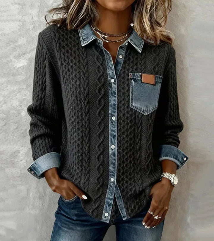 Person in a dark knit top with denim elements, standing before a textured gray surface.