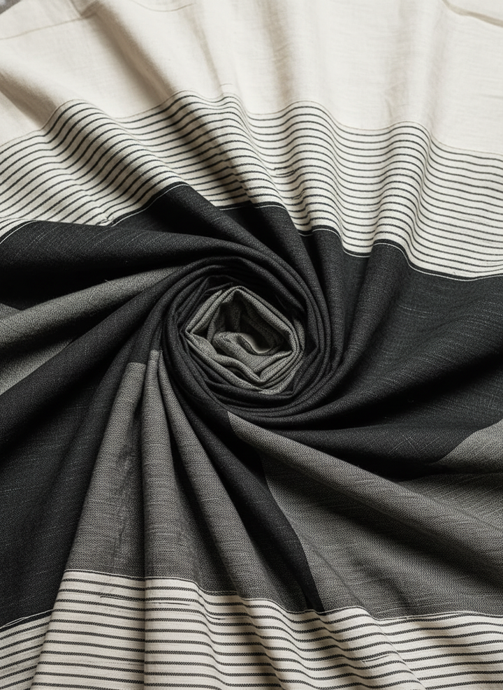 Fabric detail of a maxi dress with black, gray, and cream stripes, folded in a spiral pattern, studio setting.