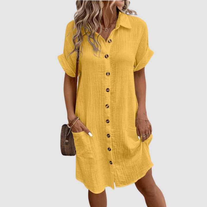 Yellow relaxed fit dress with button-down front, short sleeves, and two pockets. Worn by a model in a studio setting.