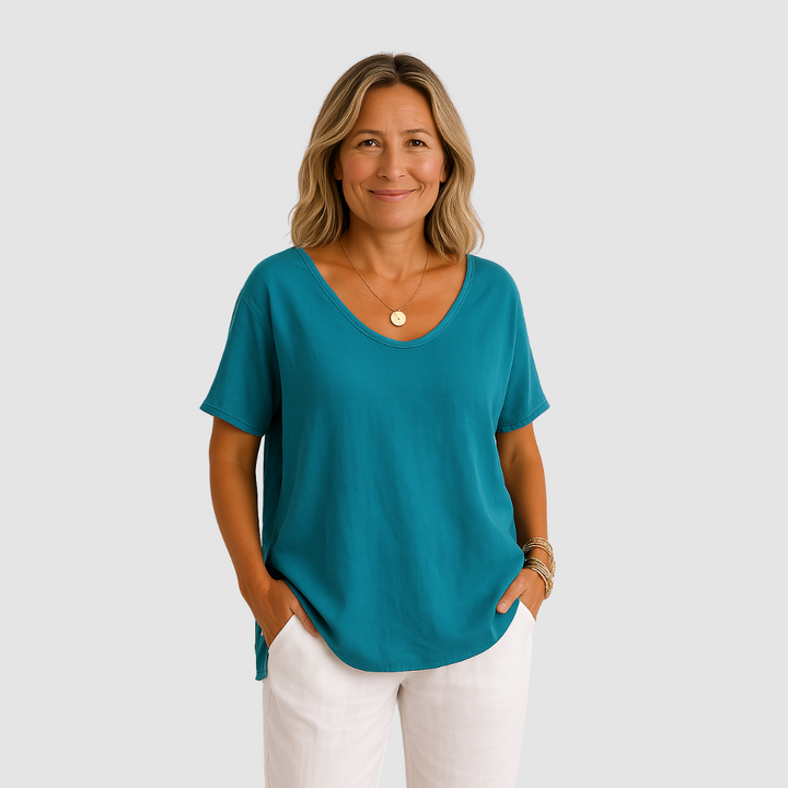 Woman in a loose fit teal t-shirt, styled with white pants against a studio backdrop.