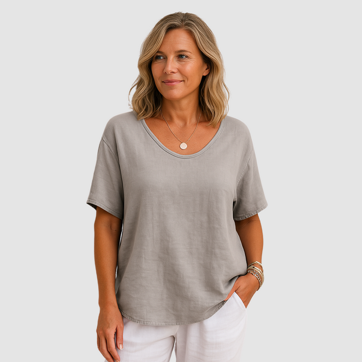 Woman in a loose fit light gray t-shirt, paired with white pants in a studio background.