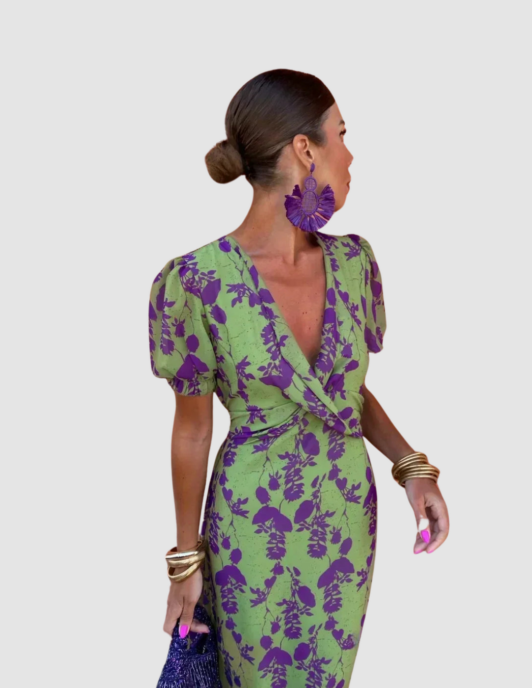 Woman wearing a green dress with purple floral print in a studio setting, accessorized with statement earrings and bracelets.