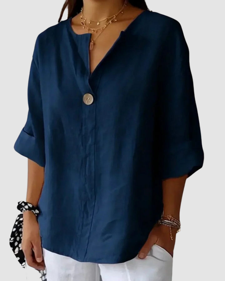 Navy blue blouse with button accent, loose and comfortable fit, rolled sleeves, styled with white pants in studio.