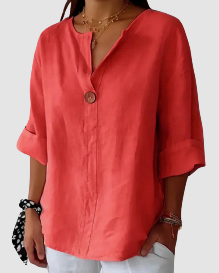 Red blouse with a wooden button, loose and flowy style, rolled sleeves, paired with white pants in a studio setting.