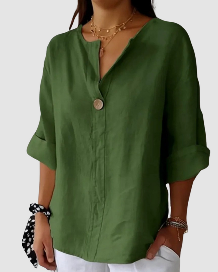 Green blouse with button detail, relaxed fit, cuffed sleeves, styled with white pants and black tie in studio.
