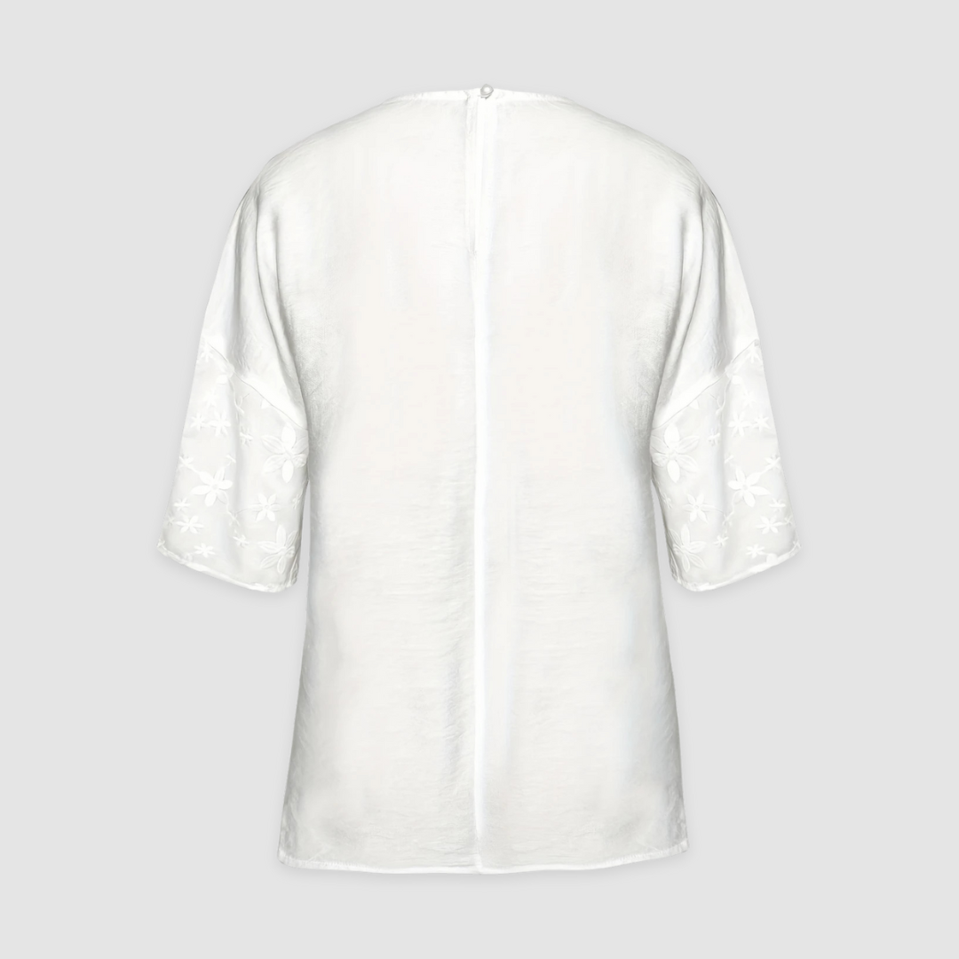 Back view of a white loose fit shirt with floral sleeves against a light gray background.