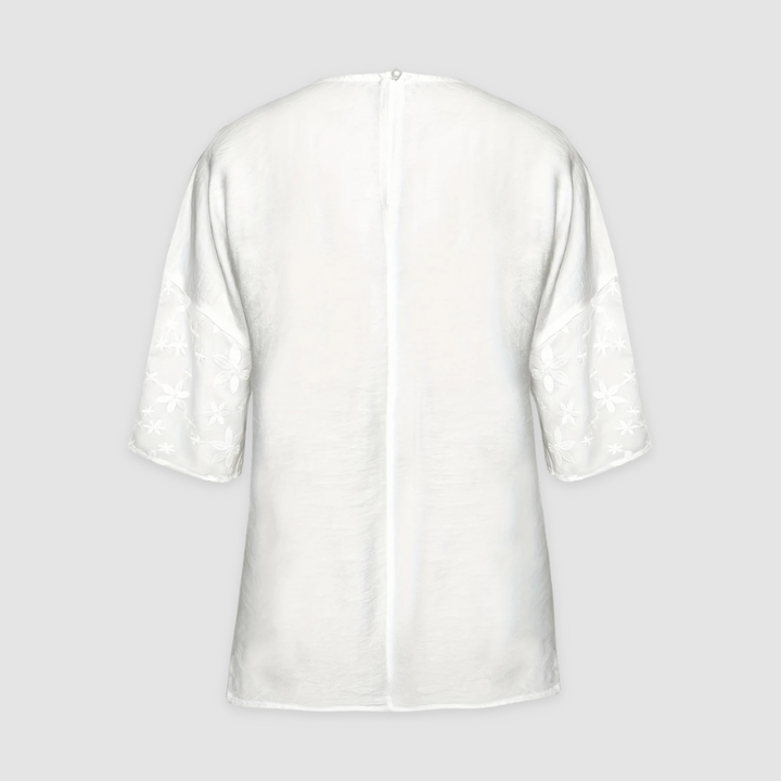 Back view of a white loose fit shirt with floral sleeves against a light gray background.