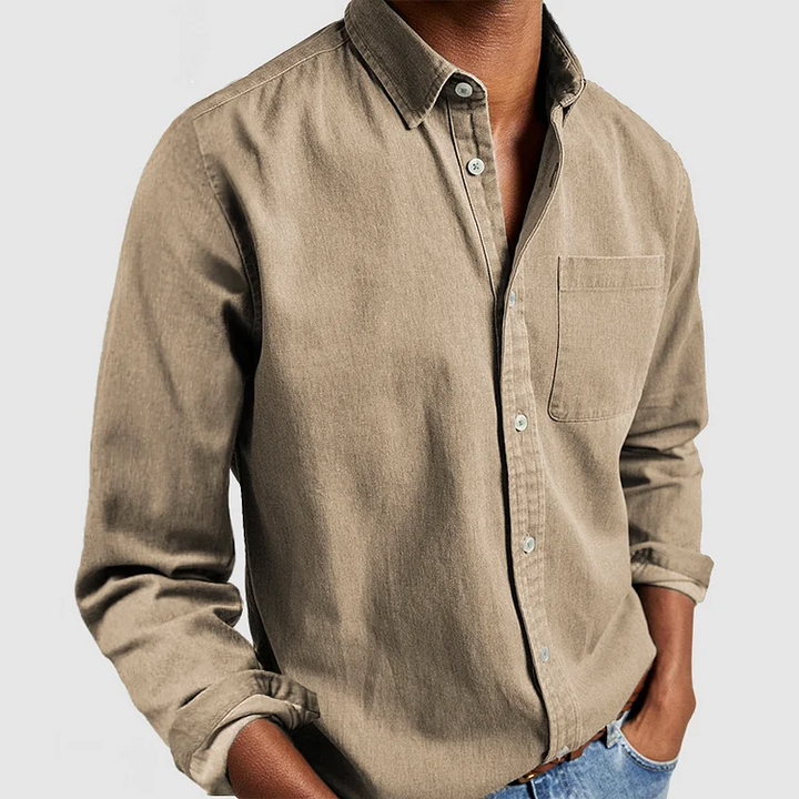Beige button-up shirt with front pocket and rolled sleeves, styled with hands in pockets; gray background.