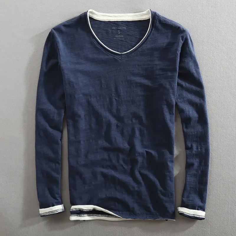 Navy long sleeve shirt with white trim, laying flat on a gray surface.