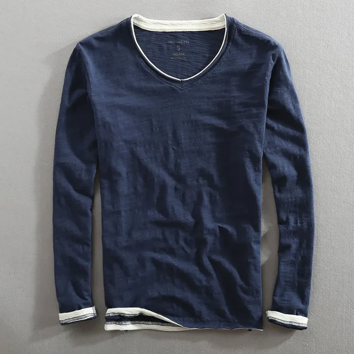 Navy long sleeve shirt with white trim, laying flat on a gray surface.