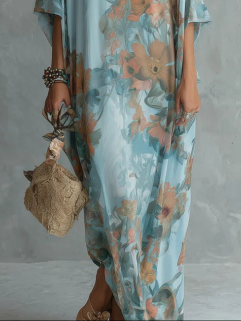 Close-up of a floral long dress in blue and orange, highlighting the lower portion with a textured handbag. Neutral textured studio backdrop.