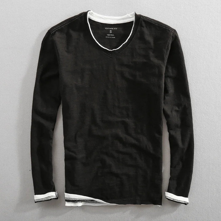 Black long sleeve shirt with white trim, laying flat on a gray surface.