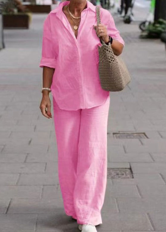 Woman dressed in a vibrant pink two-piece set with rolled sleeves, walking with a beige woven bag in an urban street.