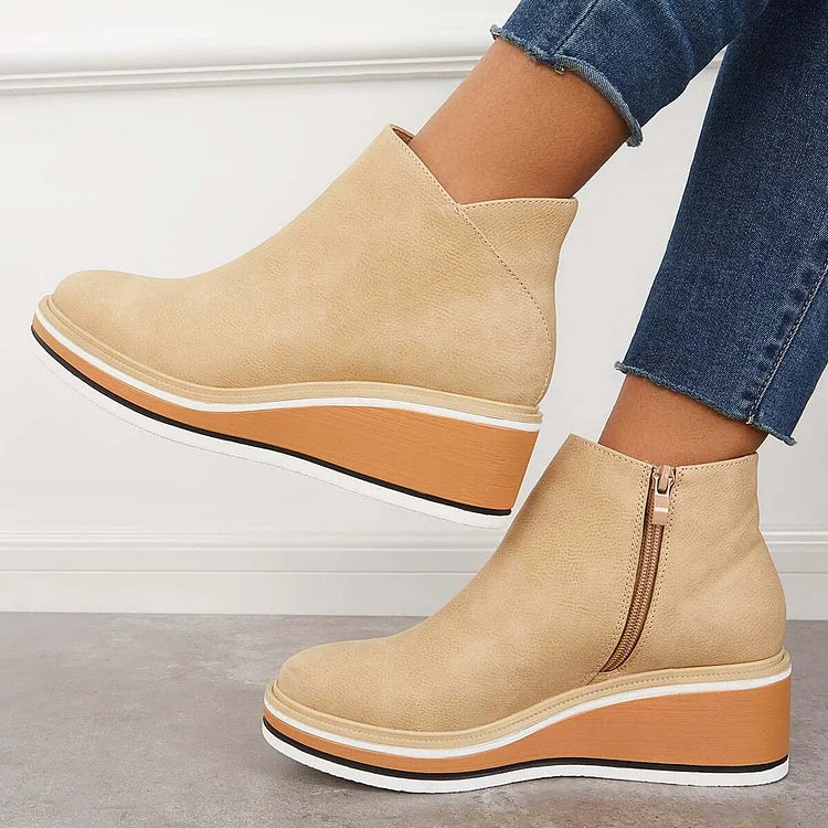 Side view of beige wedge boots with zipper, worn with jeans, against a white wall and gray floor.