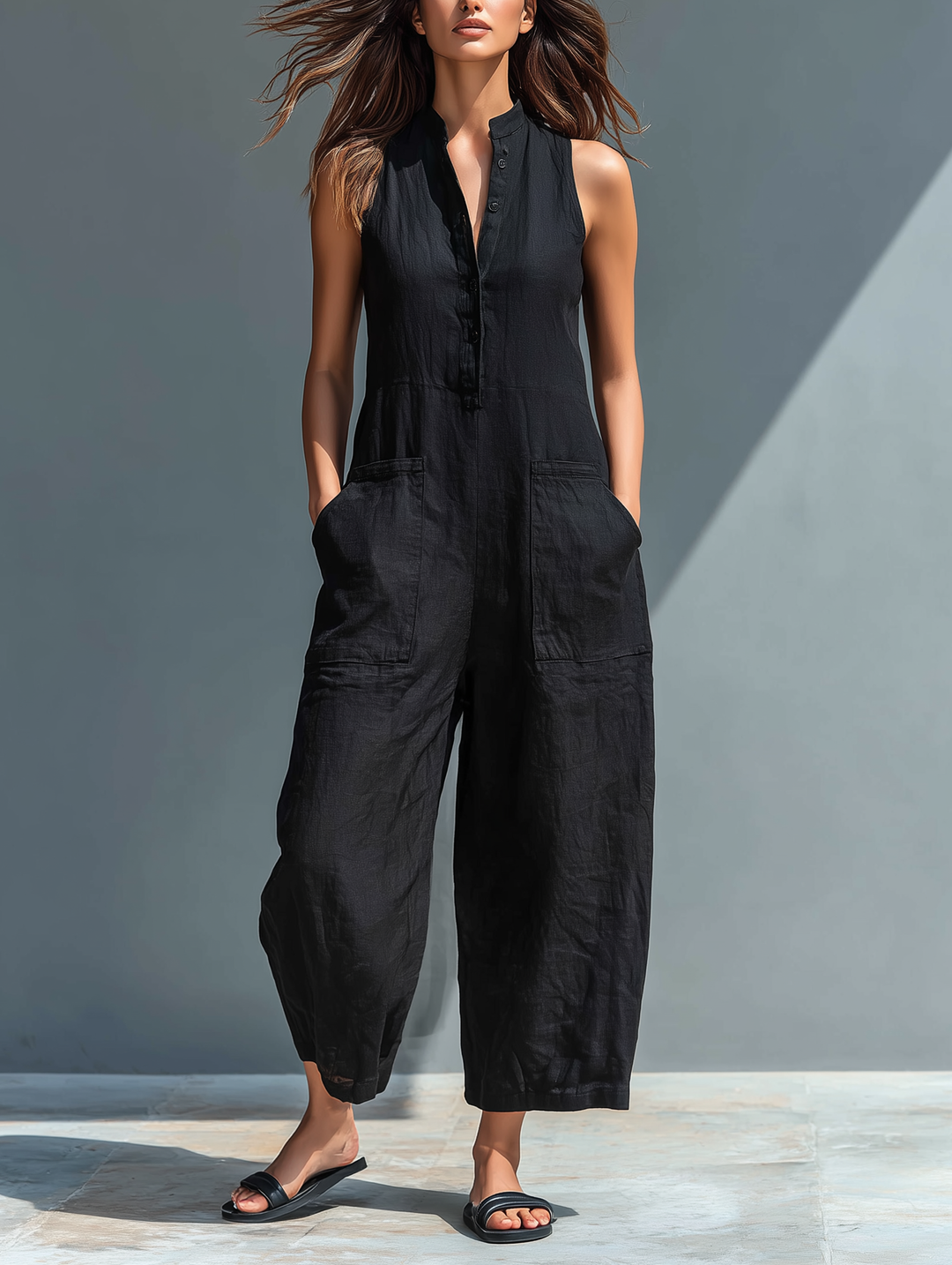 Elegant black sleeveless jumpsuit with buttoned front and pockets, worn by a woman outdoors on a sunny day.