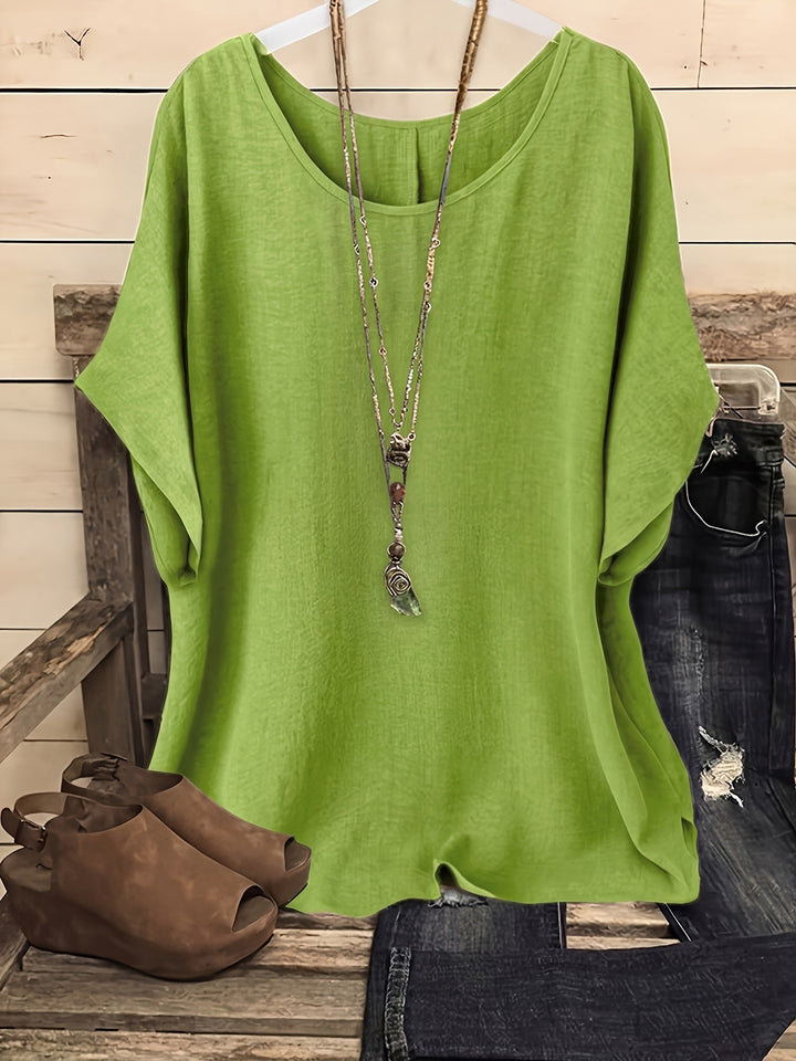 Light green loose summer top on hanger with necklace, sandals, and jeans on rustic bench.