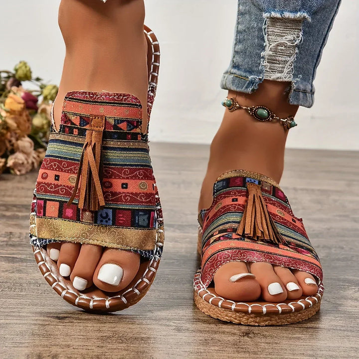 Colorful striped orthopedic sandals with tassels worn indoors on wooden floor.