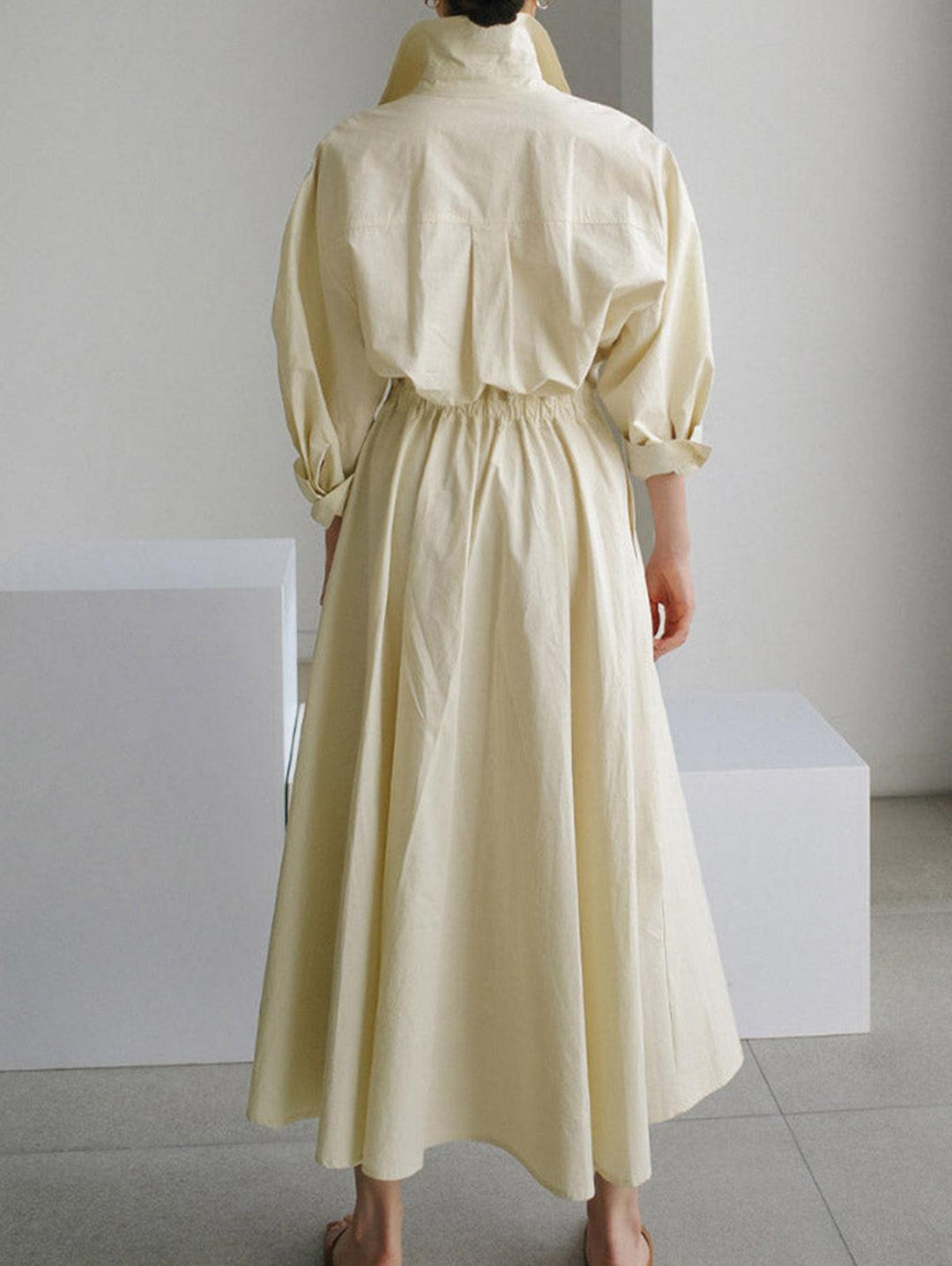 Back view of cream midi dress with button lapel and elastic waist, displayed indoors on a tile floor.