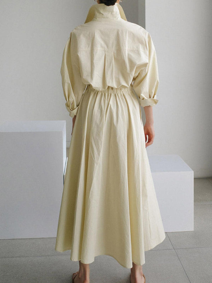 Back view of cream midi dress with button lapel and elastic waist, displayed indoors on a tile floor.