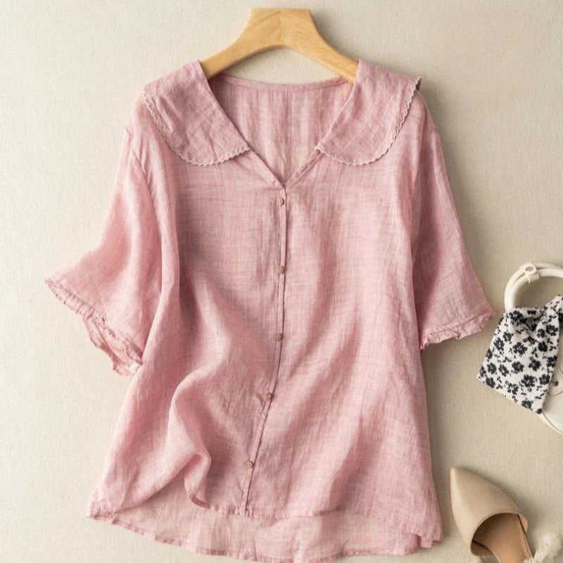 Pink short sleeve blouse with delicate trim on hanger, indoor background with shoes and handbag.