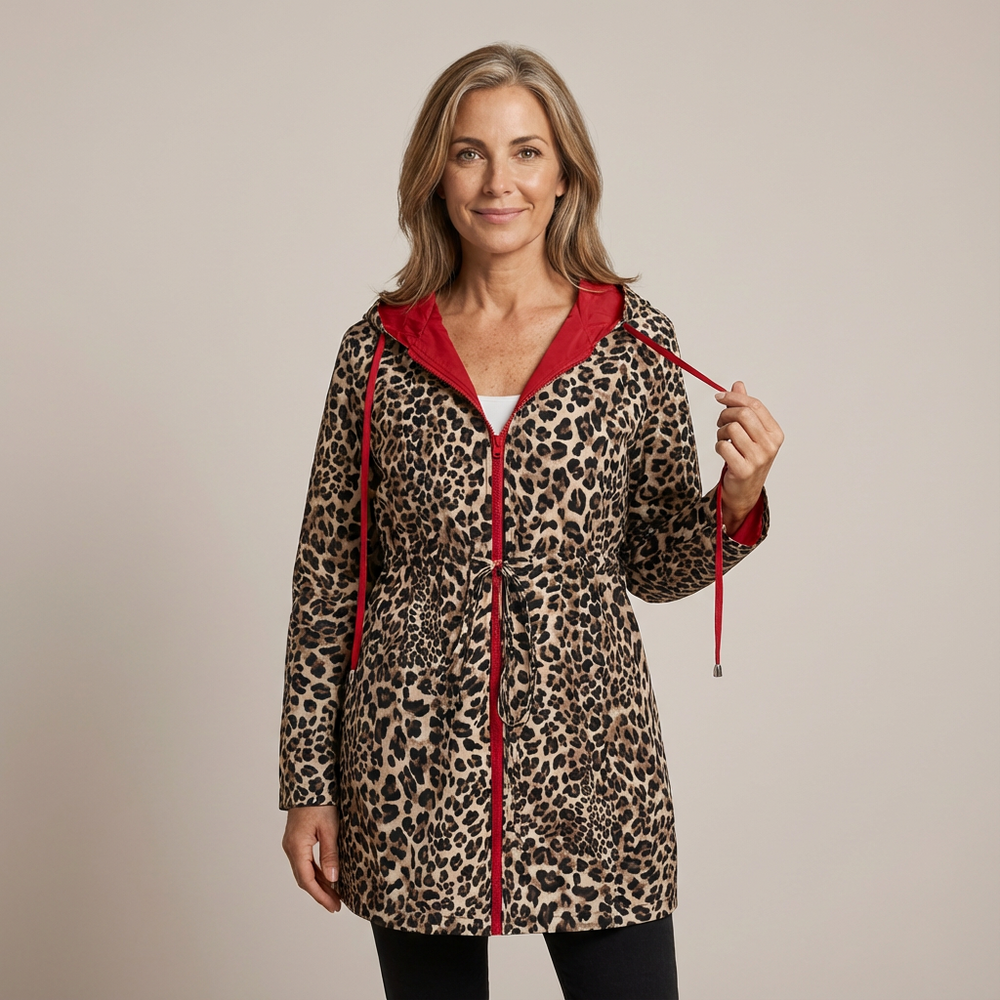 Woman wearing leopard print reversible coat with red hood, standing in a studio.