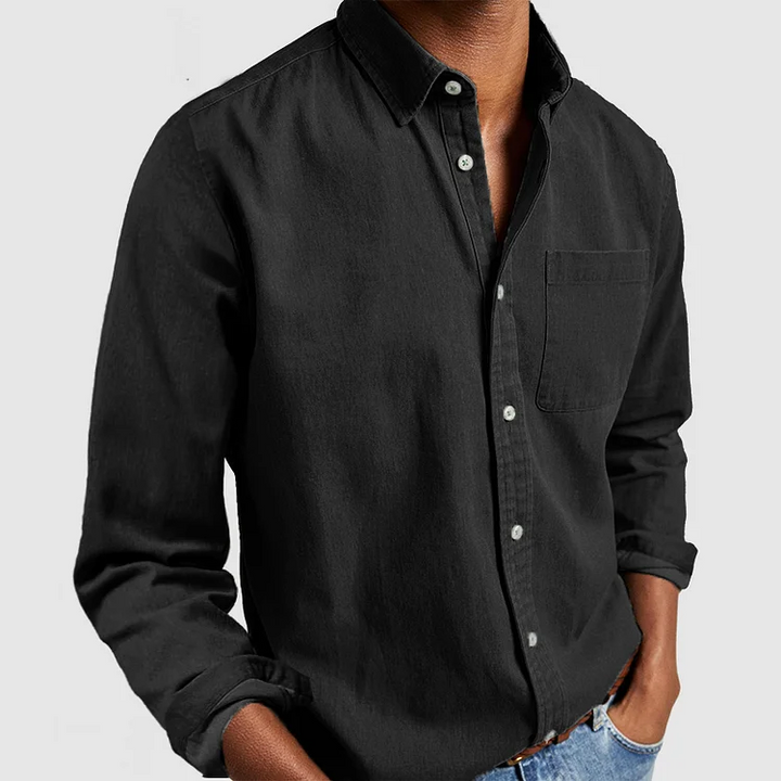 Black button-up shirt with front pocket and rolled sleeves, styled with hands in pockets; gray background.
