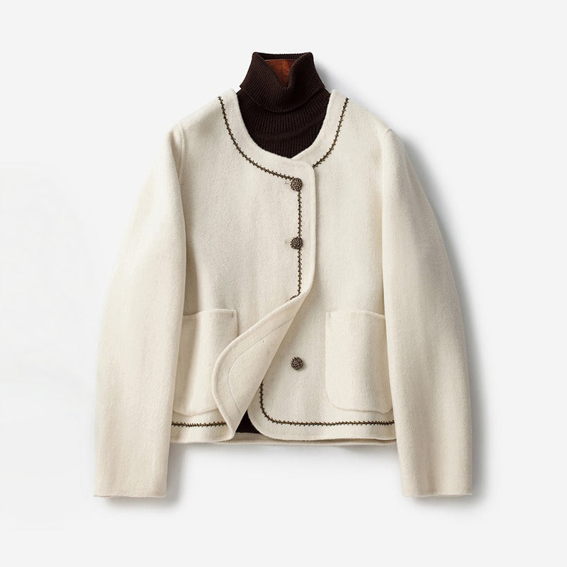 White cashmere coat with decorative trim and buttons, layered over a dark turtleneck, on a white background.