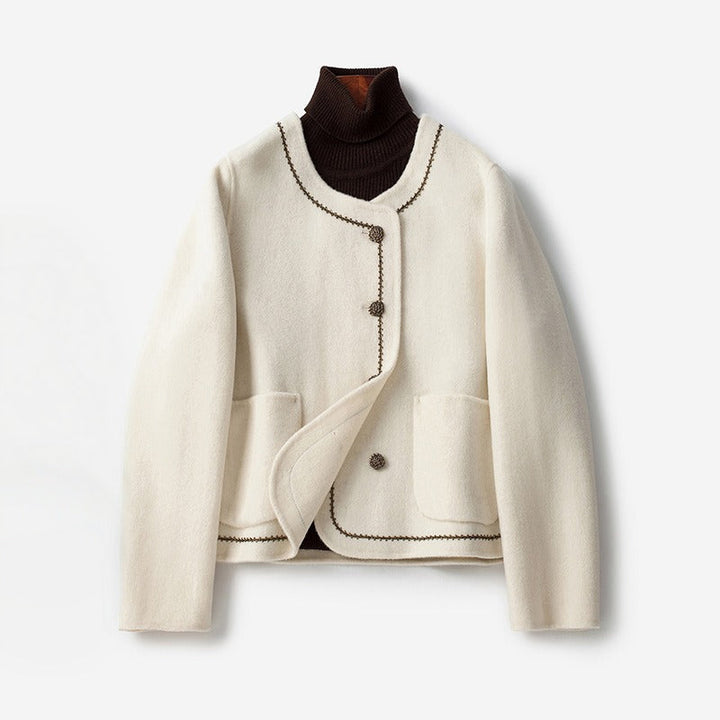White cashmere coat with decorative trim and buttons, layered over a dark turtleneck, on a white background.