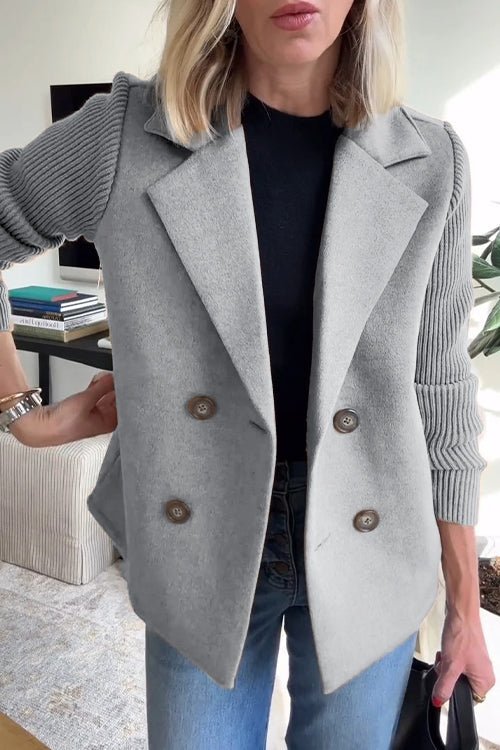 Gray knitted blazer with double-breasted buttons, worn with a black top and jeans in a bright indoor setting.