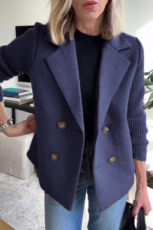 Blue knitted blazer with double-breasted buttons, worn over a black top and jeans in a well-lit indoor space.