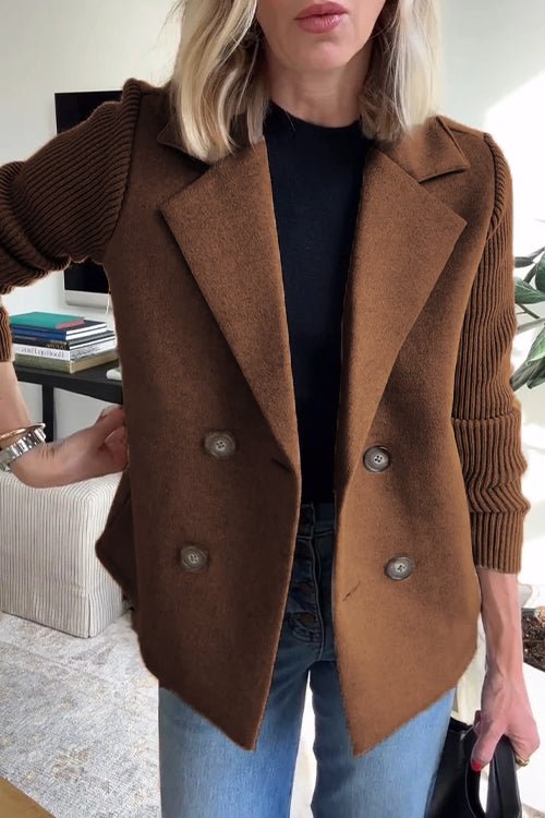 Brown knitted blazer with double-breasted buttons, worn over a black top and jeans in a bright indoor space.