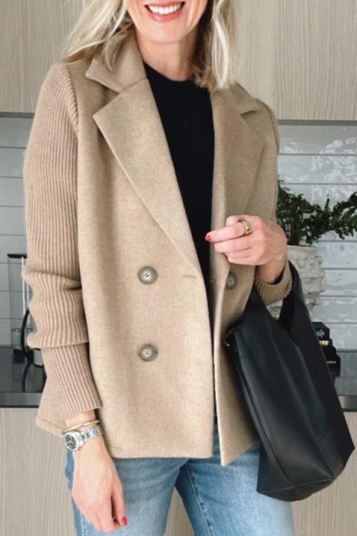 Beige knitted blazer worn over a black top and jeans, black handbag, indoors with decorative elements.