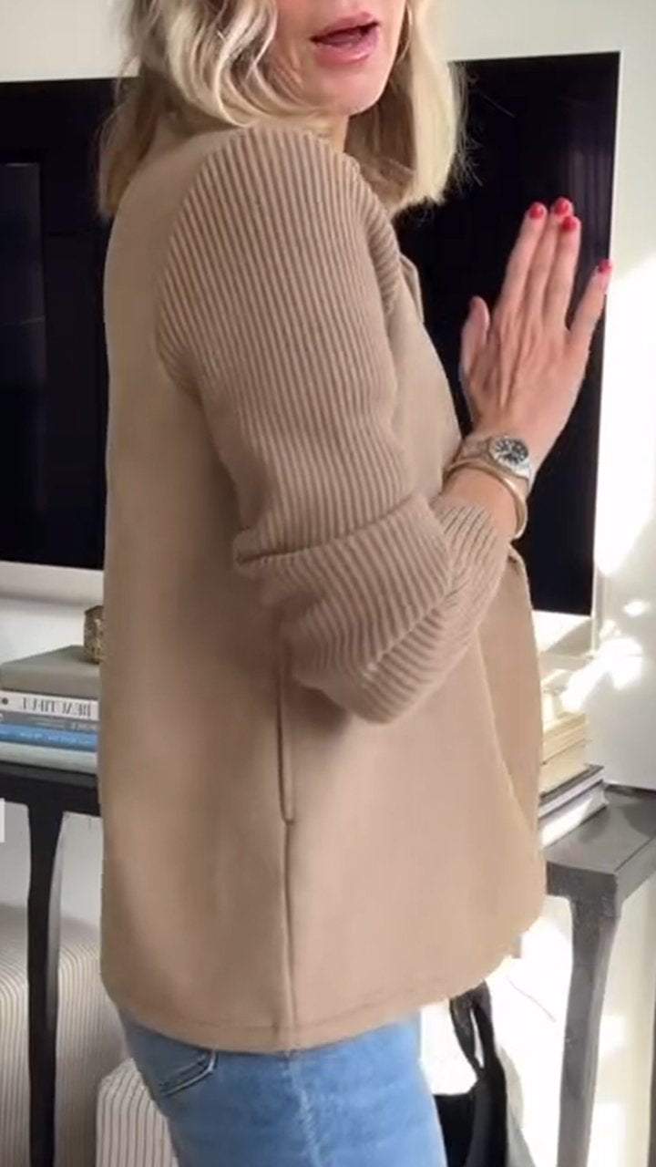 Side view of beige knitted blazer showing ribbed sleeves detail, with bright indoor background.