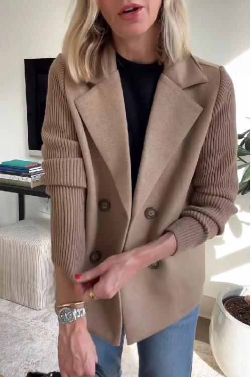 Beige knitted blazer with ribbed sleeves, worn over a black top and jeans. The setting is a bright indoor space.